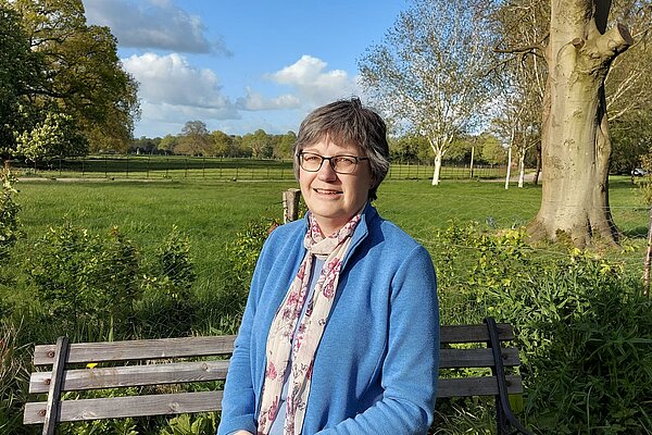 Josie Ratcliffe, sitting on a bench with a grassy field behind.